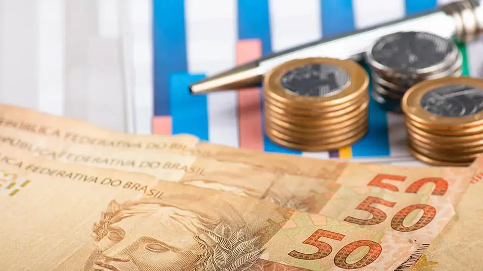 Notas de real, moedas empilhadas e gráfico de barras representando o mercado de crédito brasileiro em 2026